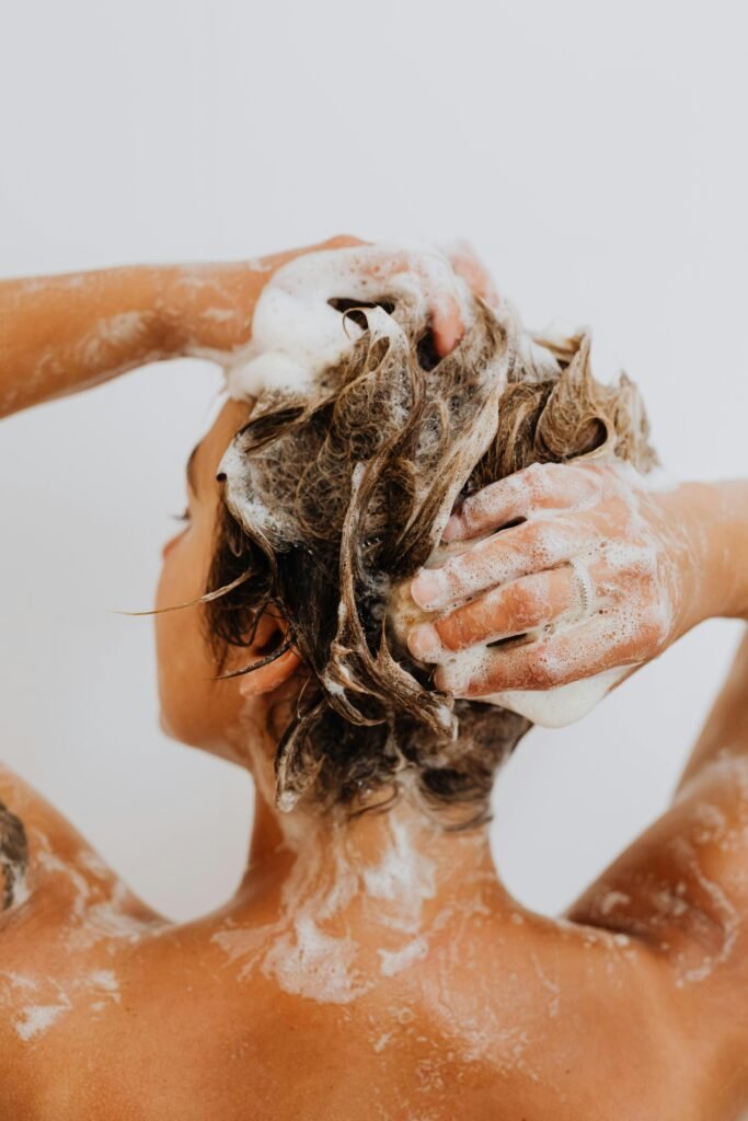 Back view of a woman washing her hair in a shower with white background. Plantas medicinales para el cabello anticaídas y brillo