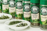 Assorted dried herbs in branded spice jars with bowls of loose herbs in the foreground.