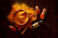 Top view of turmeric powder, curcuma roots, and essential oil on wooden surface.
