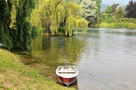 Serene river scene with a red rowboat and willow trees in Brivio, Italy.