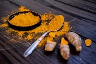 Vibrant turmeric powder and root on a dark wooden surface, emphasizing natural spices.