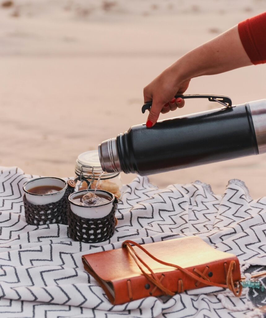 A peaceful outdoor setting with a thermos pouring tea into mugs on a blanket in the Namibian desert.