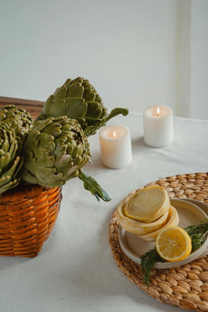 A cozy arrangement of artichokes, lemon slices, and candles on a dining table.
