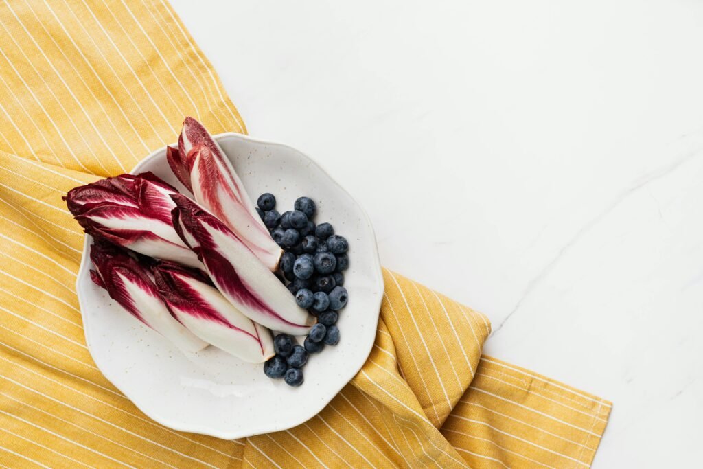 A top view of Belgian endive and blueberries on a plate placed on a yellow striped cloth.