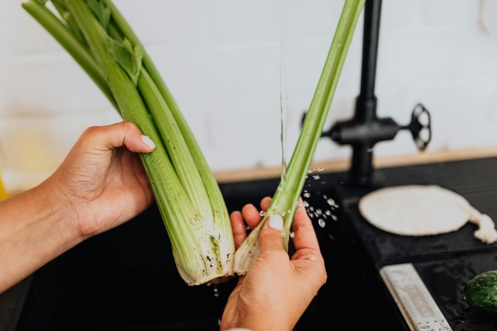 Close-up of a woman washing fresh celery in a kitchen sink, promoting healthy eating, apio

