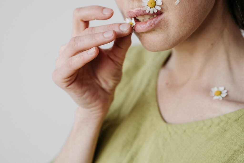 Artistic close-up of a woman with daisies on her face and hands, expressing nature and beauty.