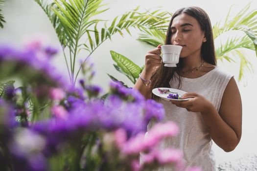 Woman savoring tea in a lush garden surrounded by vibrant flowers.
